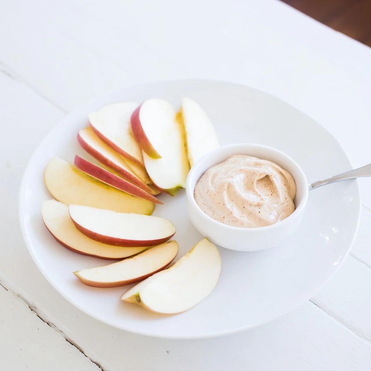 Fresh, juicy Apple Slices alongside a small bowl filled with a smooth, cinnamon-kissed peanut butter dip.
