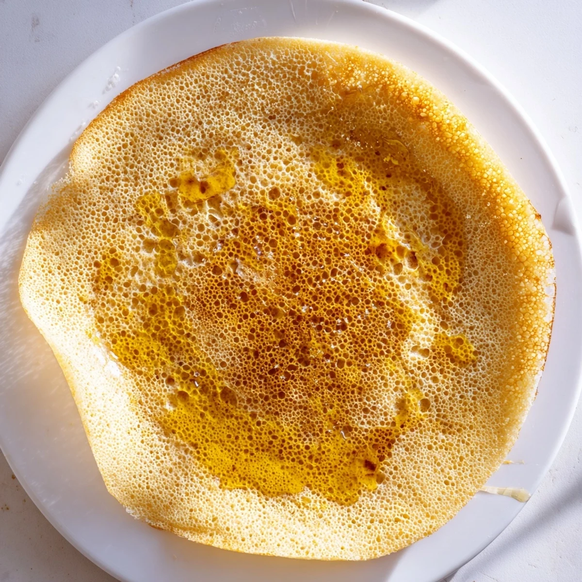 Golden, bubbly Moroccan Baghrir crepes are ready, drizzled with melted butter and sweet honey.