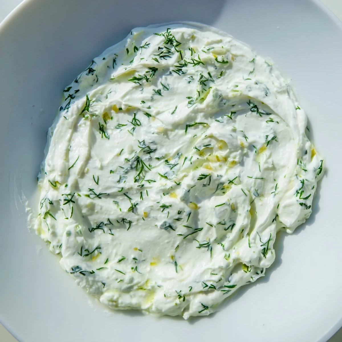 A close-up of tangy Greek Yogurt Herb Dip garnished with chopped herbs, lemon zest, and a drizzle of olive oil.