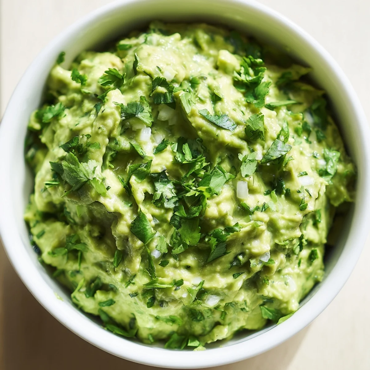 Creamy avocado lime dip in a white bowl, garnished with cilantro and lime wedges, served with tortilla chips.  