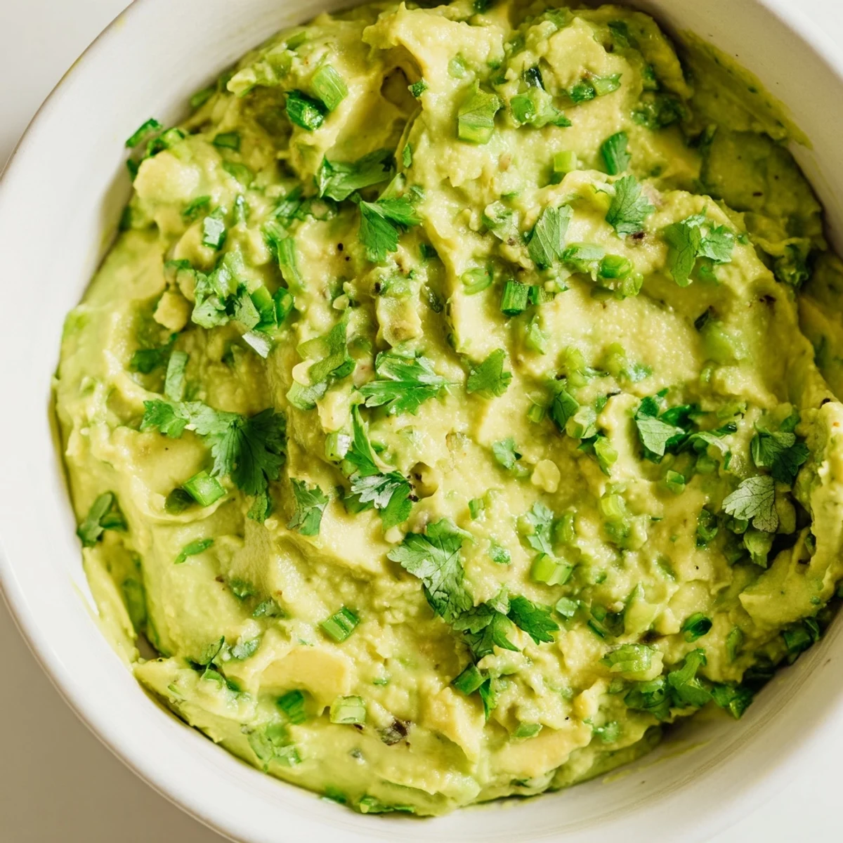 Fresh avocado lime dip topped with cilantro, surrounded by colorful veggie crudités on a rustic wooden table.  