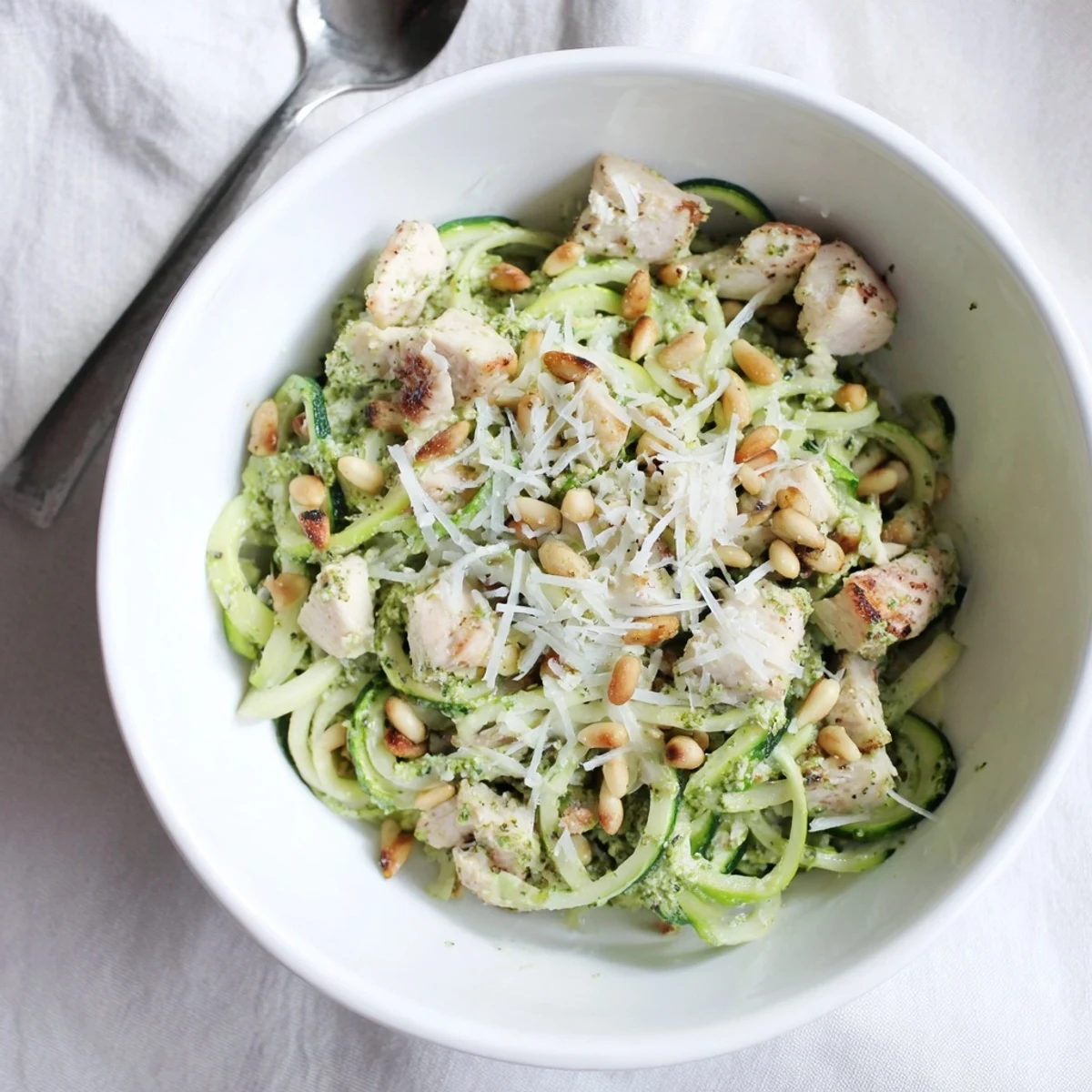 Vibrant green zucchini noodles mixed with tender chicken, drizzled with lemony pesto for a light dinner.