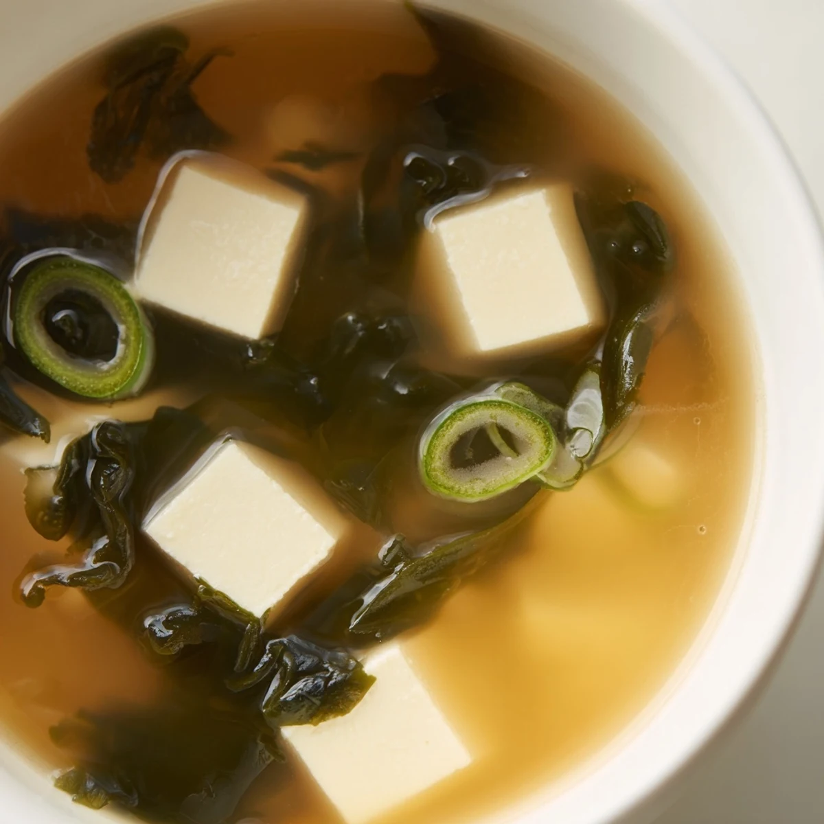 Bowl of hot Wakame Soup with silken tofu cubes, rehydrated seaweed, and fresh scallions in a clear dashi broth.  