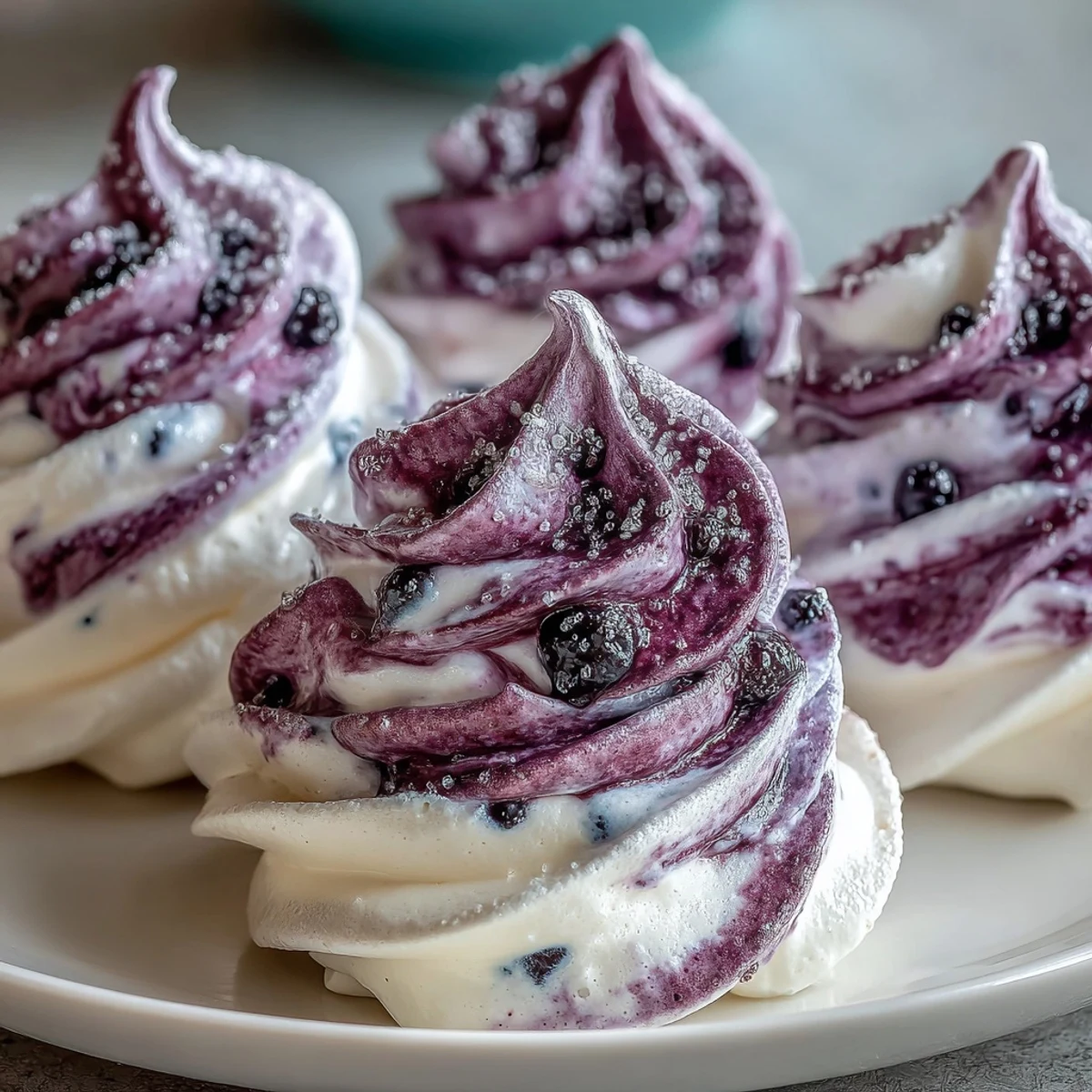 Four pale Black Currant Meringues are arranged on a white plate, offering a light and airy gluten-free dessert. 