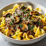 Rich, savory Slow Cooker Beef & Mushroom Gravy glistening over steaming, buttered egg noodles.