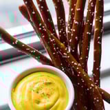 A close-up of pretzel rods with a side of spicy hot mustard dip, ideal for appetizer settings.