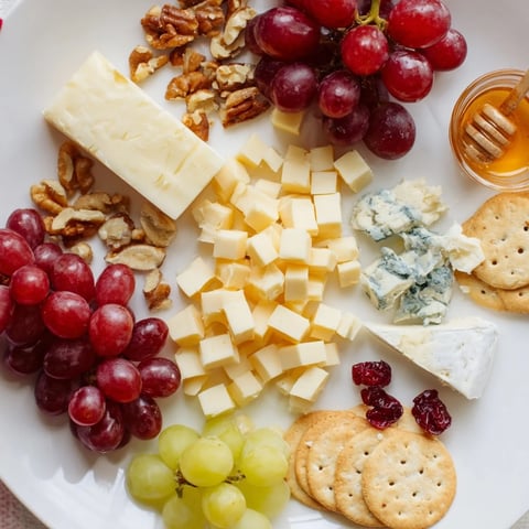 Vibrant cheese and fruit board presents the Cranberry Grape Man; cheeses, grapes, and nuts displayed beautifully.
