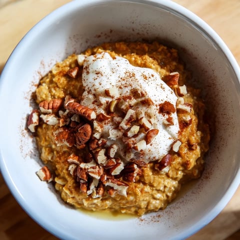 Steaming bowl of pumpkin spice latte oats with a swirl of whipped cream and pecans.