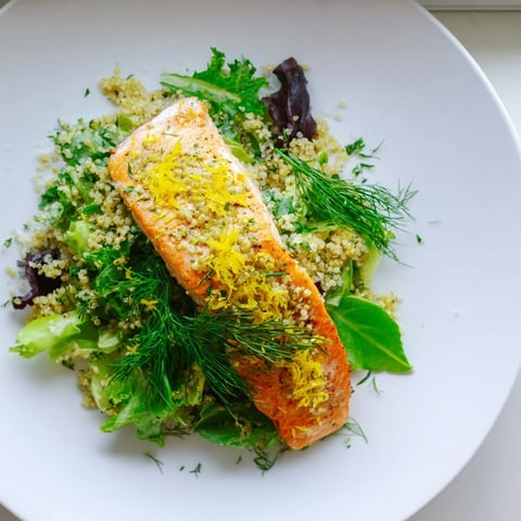 Flaky baked Lemon Herb Salmon Salad atop fluffy quinoa, fresh greens, and cherry tomatoes in a zesty citrus vinaigrette.