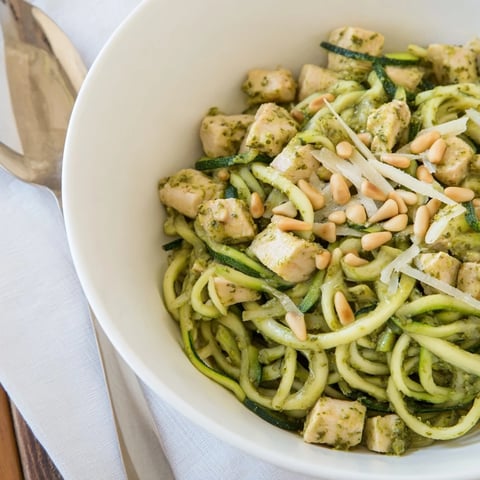Golden, sautéed chicken tossed with fresh zucchini noodles and aromatic basil pesto in a white bowl.