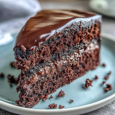 Freshly baked Easy Chocolate Fudge Cake layers sit on a wire rack, showing moist crumb and glossy ganache in a cozy home kitchen.
