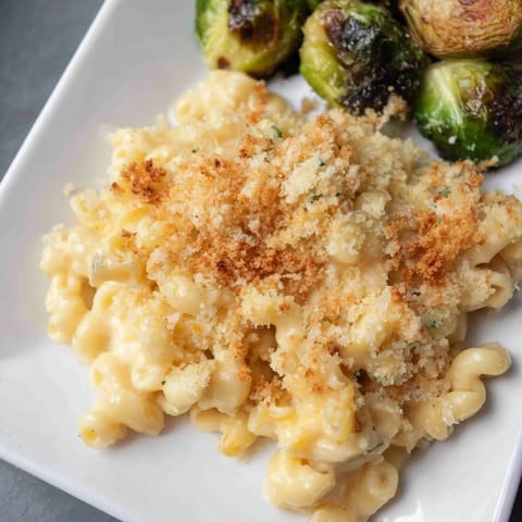A close-up of sheet pan mac and cheese, featuring bubbly cheese and crispy Brussels sprouts.