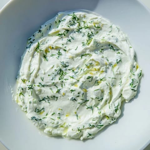 A close-up of tangy Greek Yogurt Herb Dip garnished with chopped herbs, lemon zest, and a drizzle of olive oil.