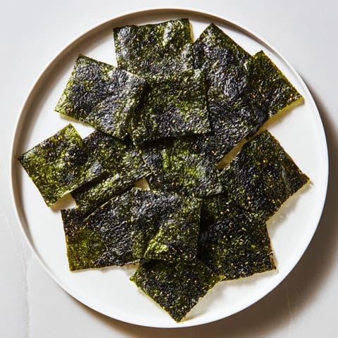 Homemade roasted seaweed chips arranged on parchment with sesame oil brushed layers, offering a crunchy, light bite ideal for vegan snacking.