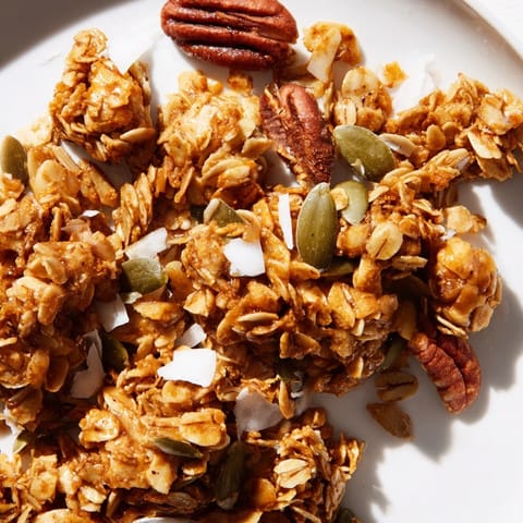 Bowl of homemade granola clusters sprinkled with cinnamon and dried cranberries, served with creamy yogurt.