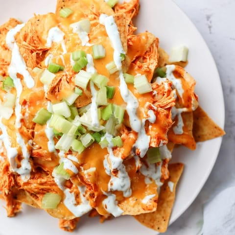 Fresh green onions and cool ranch drizzle top these baked Buffalo Chicken Nachos on a serving platter.