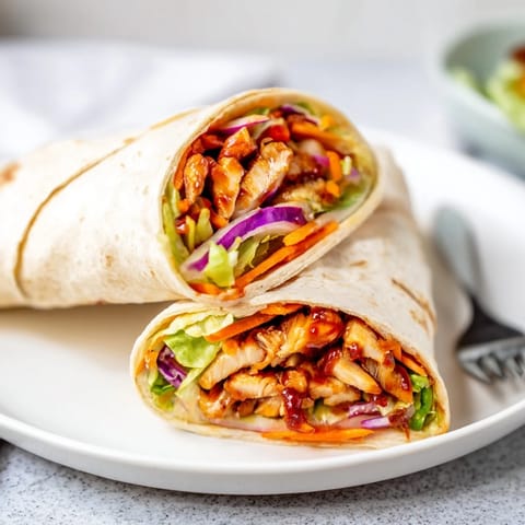 A close-up view of a Honey Sriracha Chicken Wrap cut in half, revealing layers of tender glazed chicken, julienned carrots, and fresh cilantro inside.