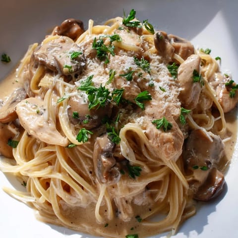 Hearty creamy mushroom chicken spaghettini plated beside a crisp green salad, highlighting the rich sauce and golden-brown chicken slices.  