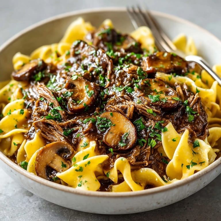Rich, savory Slow Cooker Beef & Mushroom Gravy glistening over steaming, buttered egg noodles.