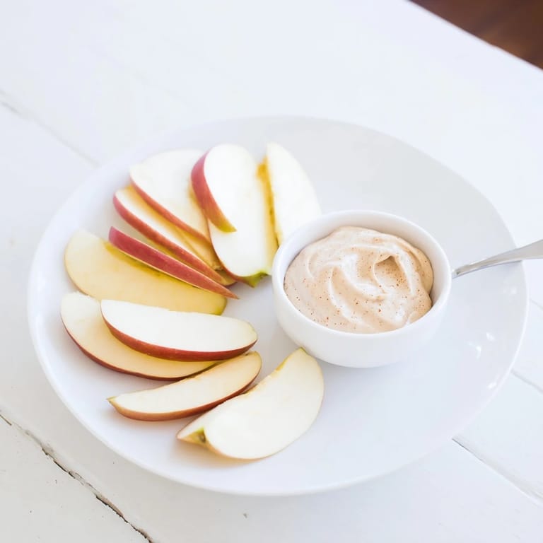 Fresh, juicy Apple Slices alongside a small bowl filled with a smooth, cinnamon-kissed peanut butter dip.