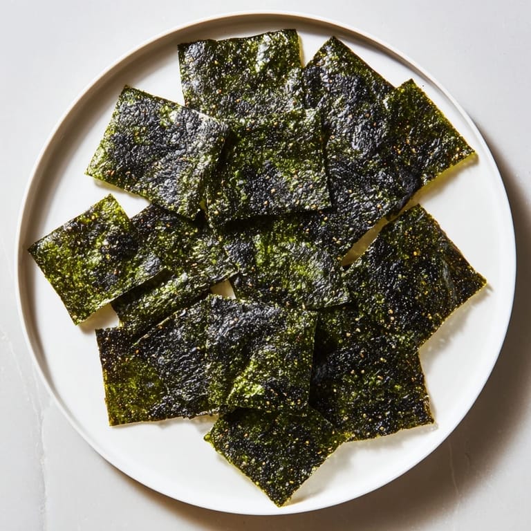 Homemade roasted seaweed chips arranged on parchment with sesame oil brushed layers, offering a crunchy, light bite ideal for vegan snacking.