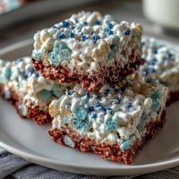 Red, white, and blue layered Rice Krispies treats with vibrant colors and sprinkles for a festive Fourth of July dessert.